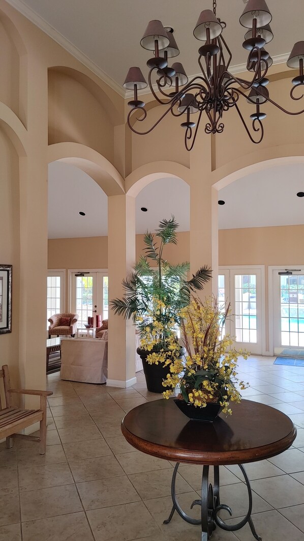 A spacious interior with a round wooden table, a chandelier, and a large potted plant with yellow flowers.