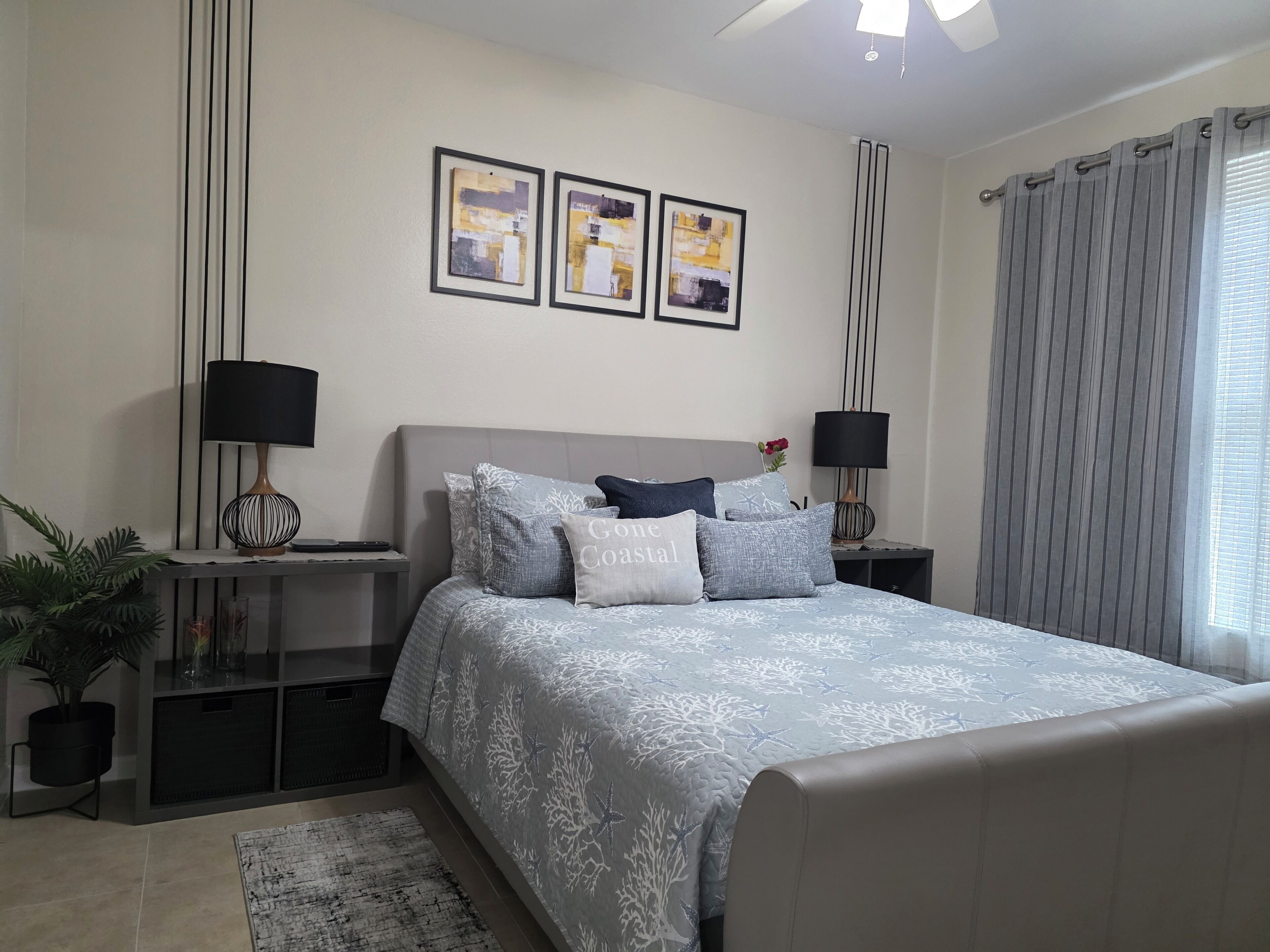 Een moderne slaapkamer met een bed, twee nachtkastjes, een potplant en kunst aan de muur.