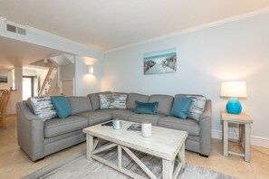 A living room with a grey sectional sofa, a coffee table, a blue lamp, and a framed picture on the wall.