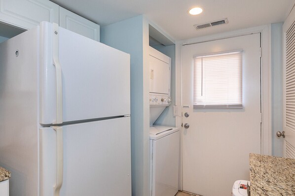A compact kitchen with a white refrigerator, a built-in oven, a washing machine, and a window with blinds. - 3 Ocean Club : Steps to the beach, pool outside your door (Hilton Head Island)