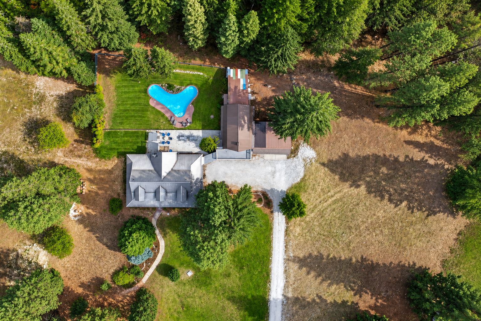 An aerial view of a property with a swimming pool, a house, and surrounding greenery.