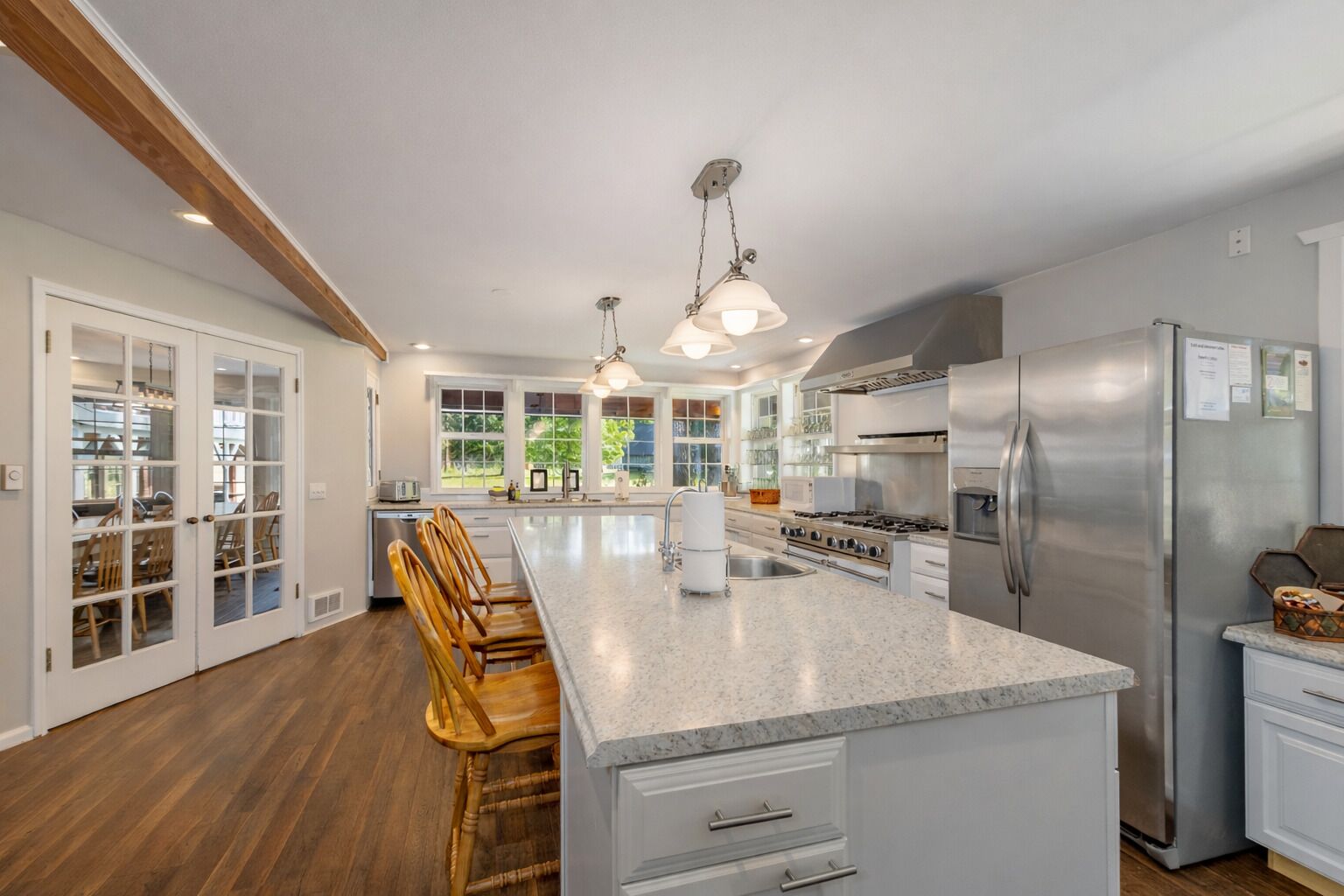 A spacious kitchen with a large island, stainless steel appliances, and a view of the outdoors through large windows.