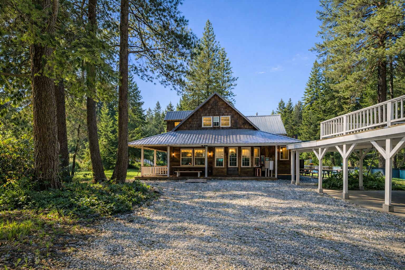A rustic cabin with a metal roof, surrounded by tall trees and a gravel driveway.