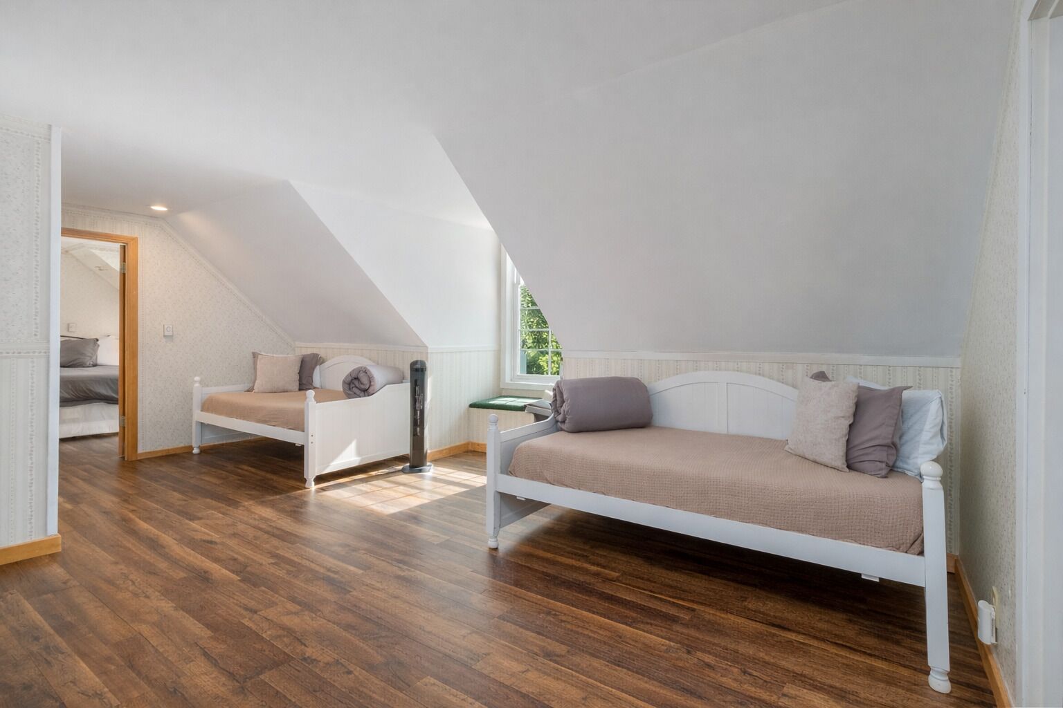 A loft bedroom with a sloped ceiling, a wooden floor, a bunk bed, and a daybed.