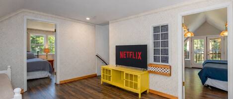 A room with a wooden floor, a bed, a yellow TV stand with a Netflix sign, and a window with a lattice design.
