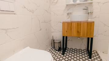 Un baño con un inodoro blanco, un tocador de madera con espejo y baldosas de suelo con diseño.