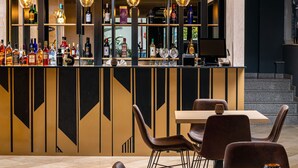 A modern bar area with a high ceiling and recessed lighting. There are multiple shelves with bottles and glasses, and a bar counter with a computer. The seating area includes a wooden table and several upholstered chairs. - Labirint Hotel (Bucharest)