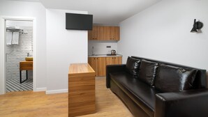 A modern living space with a wooden dining table, a black leather sofa, and a kitchen area with wooden cabinets and a flat-screen TV. - Labirint Hotel (Bucharest)