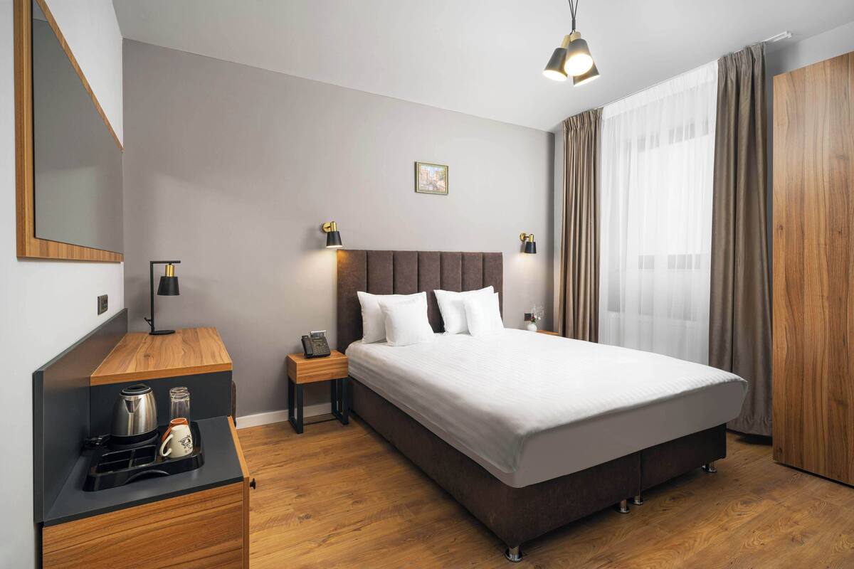 A neatly arranged hotel room with a large bed, bedside tables, a coffee maker, and a mirror.