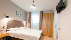 A hotel room with a bed, bedside table, lamp, TV, and a wooden wardrobe. - Labirint Hotel (Bucharest)