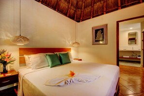 A hotel room with a bed, a nightstand, a vase with flowers, a framed picture on the wall, and a bathroom visible through an open door.