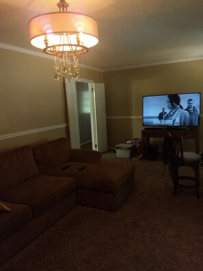 Relax in this inviting living room with a comfortable sofa, coffee table, and TV on a stand, plus a chandelier above.