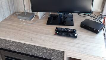 Una scrivania in legno con un monitor a schermo piatto, una lampada, una tastiera, un telecomando e un router.