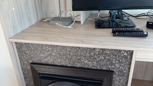 A modern living room with a fireplace, a flat-screen TV, and a set of remote controls. - Beautiful mobile home close to the beach and the sea. (IJmuiden)