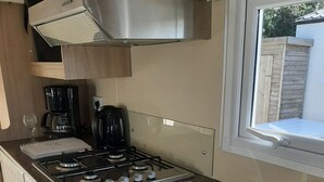 A compact kitchen with a gas stove, coffee maker, and a stainless steel sink. - Beautiful mobile home close to the beach and the sea. (IJmuiden)