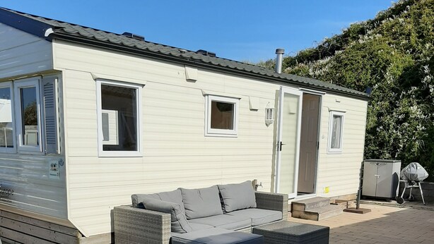 A mobile home with a patio area, including a sofa, cushions, and two large flower pots. - Beautiful mobile home close to the beach and the sea. (IJmuiden)