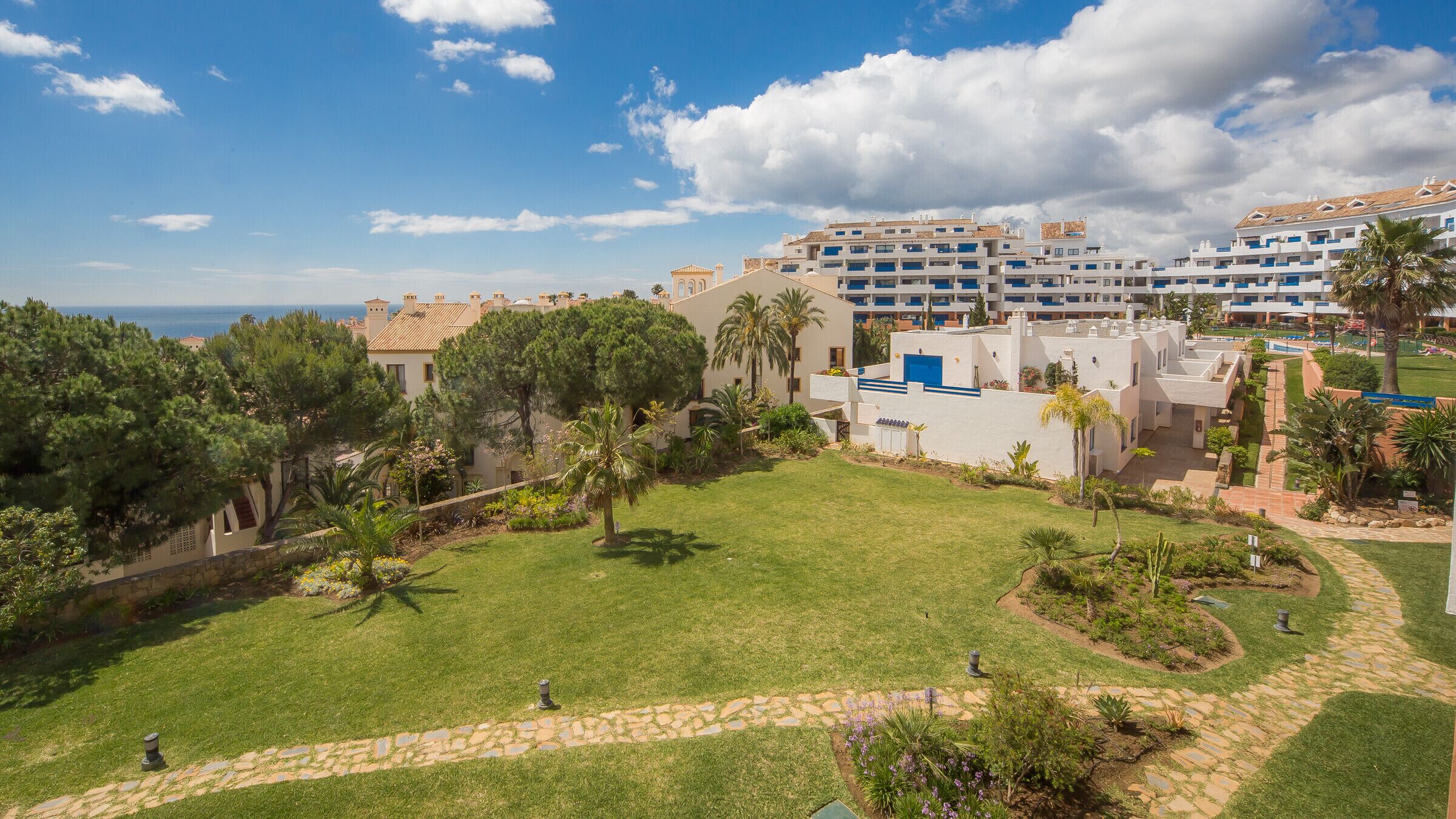 A resort with multiple buildings, a well-maintained lawn, and a clear view of the sea.