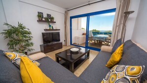 Una sala de estar con sofá, mesa de centro, televisor y vistas al exterior.