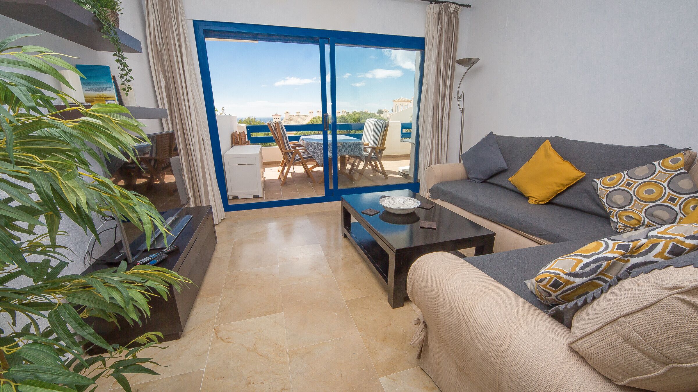 A living room with a sofa, coffee table, and a view through a glass door to the outside.