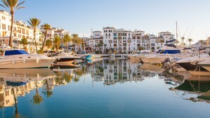 Un port esportiu amb embarcacions amarrades, envoltat d'edificis d'altes plantes amb balcons, palmeres i cel blau.