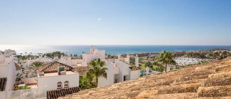 A coastal town with white buildings, a rocky hillside, and a view of the sea.
