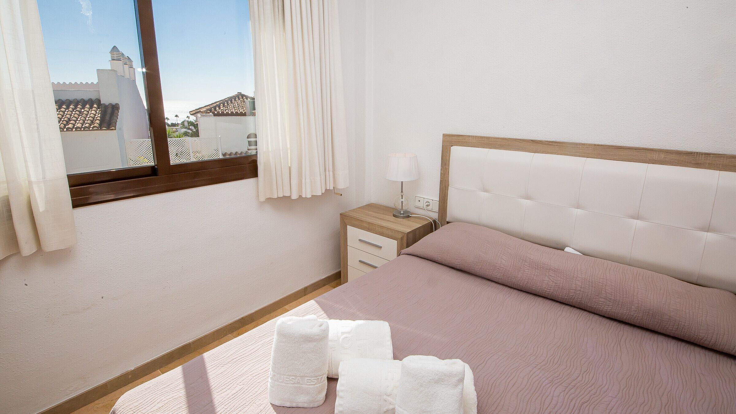 A bedroom with a bed, a nightstand, a lamp, and a window with curtains.