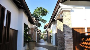 A narrow, paved pathway flanked by buildings with stone and brick facades, leading to a gated area. - Wonderland Villa at Port Dickson (Port Dickson)