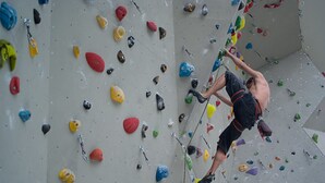 Eine Person erklimmt eine Kletterwand mit farbig markierten Griffen.