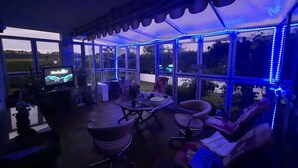 Eine überdachte Terrasse mit Fernseher, Sitzgelegenheiten und Blick ins Freie.