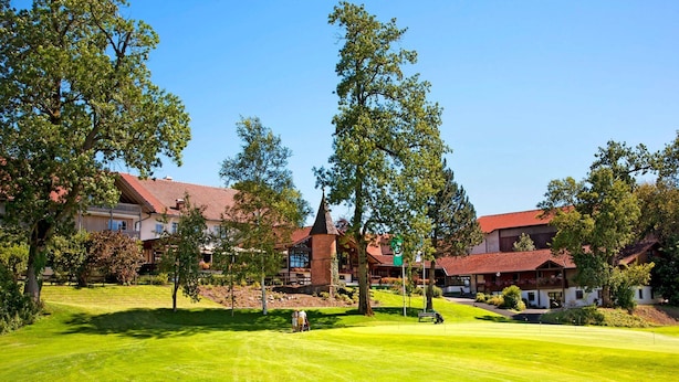 Ein Golfplatz mit Clubhaus, umgeben von Bäumen und Gebäuden mit roten Dächern.