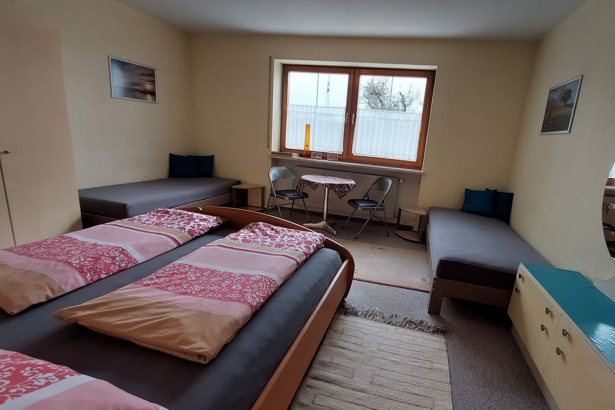 A room with two single beds, a small desk, a chair, and a window.