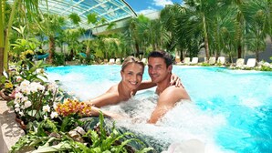 Ein Paar in einem Pool mit Glasdach und tropischen Pflanzen.