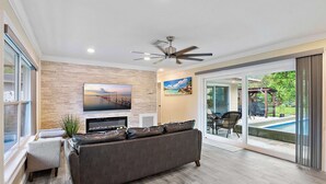 Ein Wohnzimmer mit Flachbildfernseher, Deckenventilator und Blick auf einen Pool durch Glastüren.