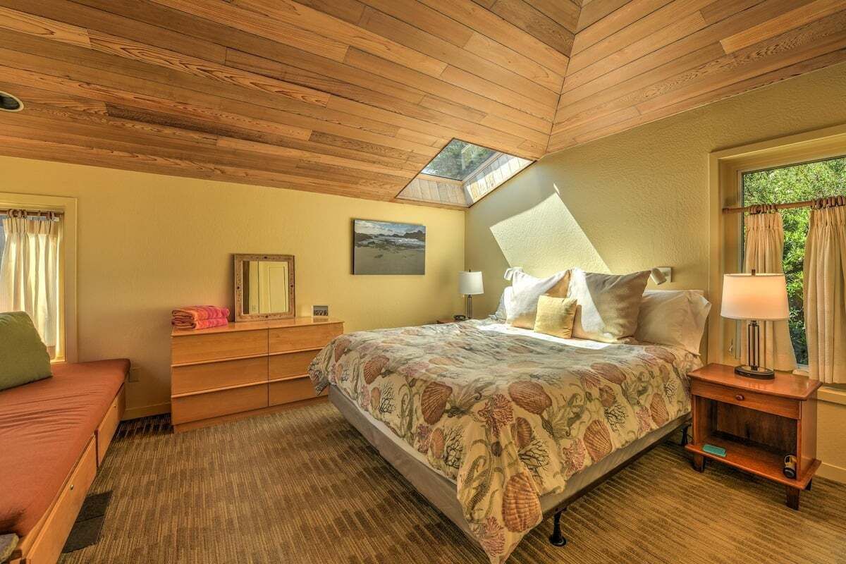 Ein Schlafzimmer mit einem Bett, Nachttischen, einer Bank und einem Fenster mit Vorhängen.