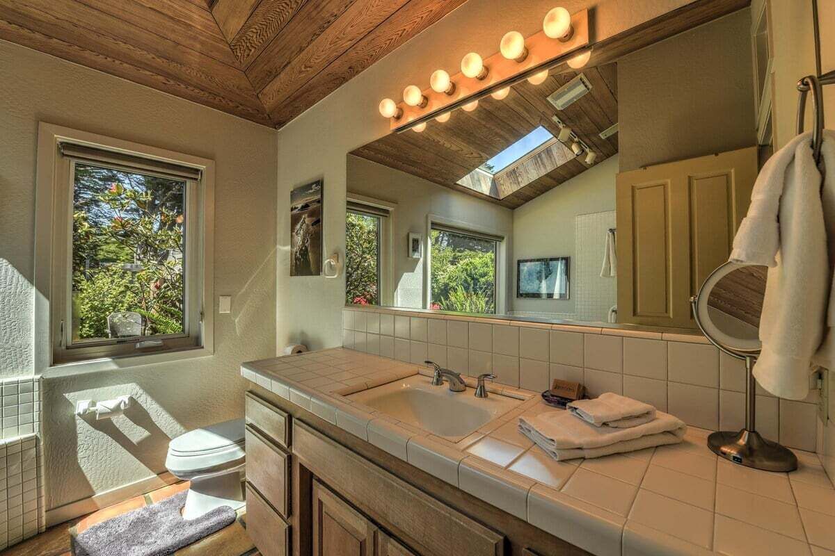 A bathroom with a wooden ceiling, a large mirror, a sink, and a window.