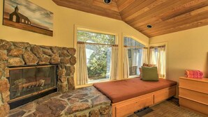 A cozy room with a stone fireplace, a bed with a green pillow, and a wooden dresser. - Wild Moor - Hot Tub & Star View Retreat (Sea Ranch)