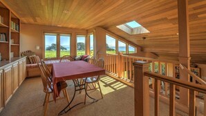 A dining area with a table and chairs, a bookshelf, and a view of the outdoors. - Wild Moor - Hot Tub & Star View Retreat (Sea Ranch)