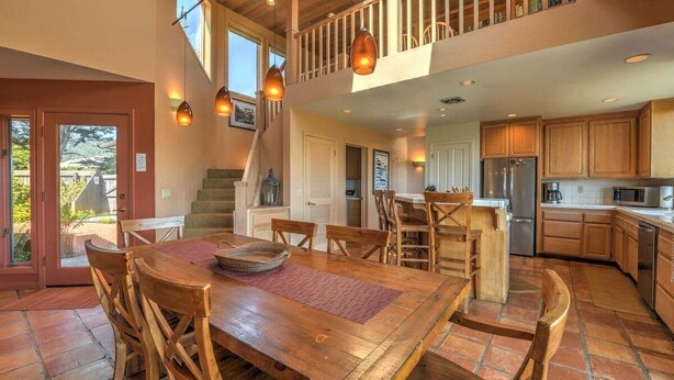A spacious kitchen with wooden cabinets, a dining area with a large wooden table and chairs, and a staircase leading to an upper level. - Wild Moor - Hot Tub & Star View Retreat (Sea Ranch)