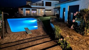 A swimming pool with a stone pathway leading to a house with a blue exterior and a visible garage door. - Sítio do Louro Villa - Deluxe Villa w/ gaming room (São Martinho do Porto)