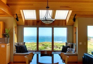 Comedor con mesa y sillas, ventanas amplias con vistas al océano y un techo con tragaluces.