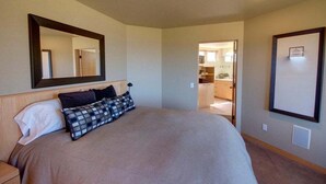 A bedroom with a large bed, a mirror, and a view into the kitchen. - Galleon's Reach- Pebble Beach & Black Point Access (Sea Ranch)