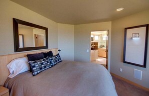 Ein Schlafzimmer mit einem großen Bett, einem Spiegel und Blick zur Küche.