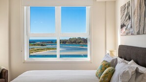 Ein Schlafzimmer mit einem großen Fenster mit Blick auf einen Strand und eine felsige Küste.