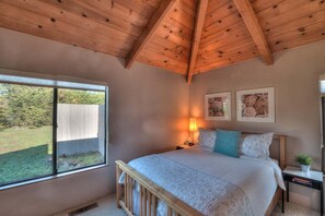 A bedroom with a wooden ceiling, a large window, and a bed with a white bedspread and pillows. - Point of View | Dog-Friendly Oceanfront Escape (Sea Ranch)