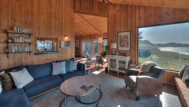 Ein geräumiges Wohnzimmer mit großem Fenster, Holzwänden, einem blauen Sofa und einem Couchtisch.