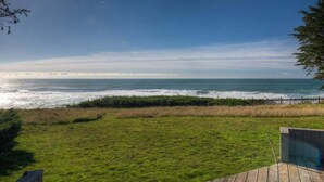 Eine Rasenfläche mit einer Holzterrasse und Blick auf das Meer.