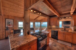 A kitchen with wooden cabinets, granite countertops, a stove, and a large window overlooking the ocean.