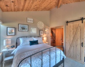 A bedroom with a bed, bedside tables, wall art, and a wooden door. - Point of View | Dog-Friendly Oceanfront Escape (Sea Ranch)