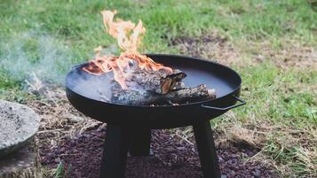 Una parrilla portátil negra con llamas visibles y leña ardiendo, sobre una superficie cubierta de césped.