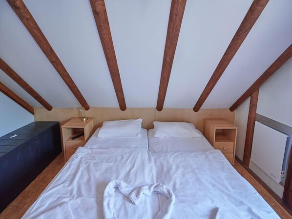 Un dormitorio con techo de madera, una cama con ropa de cama blanca, dos mesitas de noche y un tocador.